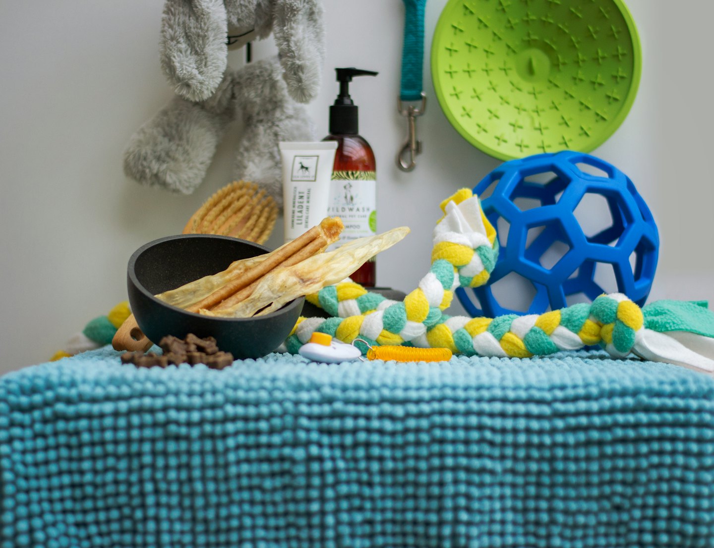 Assorted pet care products, treats, and toys on a blue mat.
